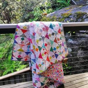 May include: A colorful patchwork quilt with a variety of geometric patterns and bright colors, folded and draped over a wooden railing.