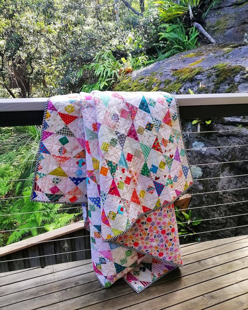 May include: A colorful patchwork quilt with a variety of geometric patterns and bright colors, folded and draped over a wooden railing.