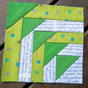 May include: A green and yellow patchwork quilt block with a white fabric background featuring a repeating pattern of handwritten text and small clover designs. The text includes the phrases "Dream without fear", "Love without limits", "Dream big", "Be grateful", "Follow your dreams", "Give love", "Laugh lots", "Don't quit yourself", "Dream a little dream", "Dream it", "Wish it", "Do it", and "Follow your dreams, they're half way there".