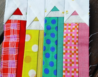 May include: Five colorful fabric pencil blocks sewn together. The pencils are red, yellow, green, blue, and pink. Each pencil has a white triangle at the top and is made of different patterned fabrics.