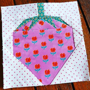 Peut inclure: Un carré de tissu rose avec un fond blanc et des pois roses. Au centre du carré se trouve un cœur en tissu rose avec un motif floral orange et bleu. Le cœur est recouvert d'un tissu vert avec un motif floral blanc.