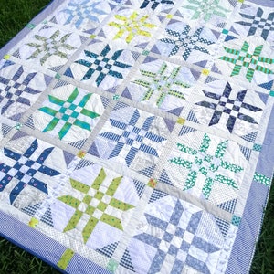 May include: A patchwork quilt with a blue border and a white background. The quilt is made up of various squares with different patterns, including blue and white gingham, floral prints, and geometric designs. The quilt is made with a variety of fabrics, including cotton and linen.