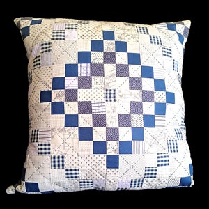 May include: A square patterned pillow with a blue and white design. The pillow is made of fabric with a variety of patterns, including plaid, stripes, and polka dots.