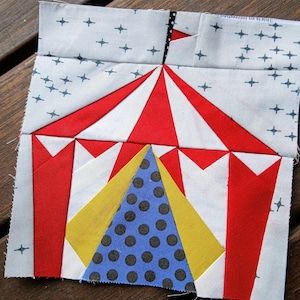 Może przedstawiać: Namiot w czerwono-białe pasy z niebieskim i czarnym środkiem w kropki. Namiot znajduje się na białym tle z niebieskimi gwiazdami.