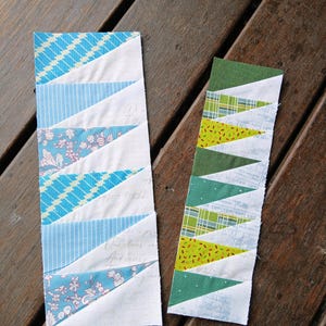Pode incluir: Duas tiras de tecido com um design de patchwork. Uma tira apresenta triângulos estampados azuis e brancos, enquanto a outra tem triângulos verdes e amarelos. As tiras estão sobre uma superfície de madeira.