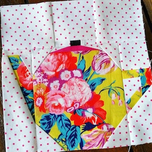 Puede incluir: Un bloque de colcha de retazos con una tela floral en el centro y tela blanca con lunares rosas alrededor de los bordes.