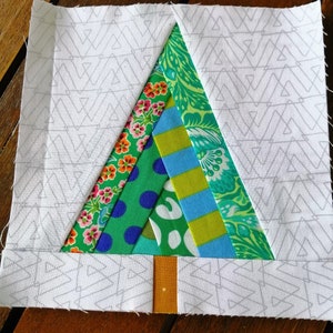 May include: A patchwork fabric Christmas tree with a brown trunk. The tree is made of green, blue, yellow, pink, and white fabric. The background is white with a gray chevron pattern.