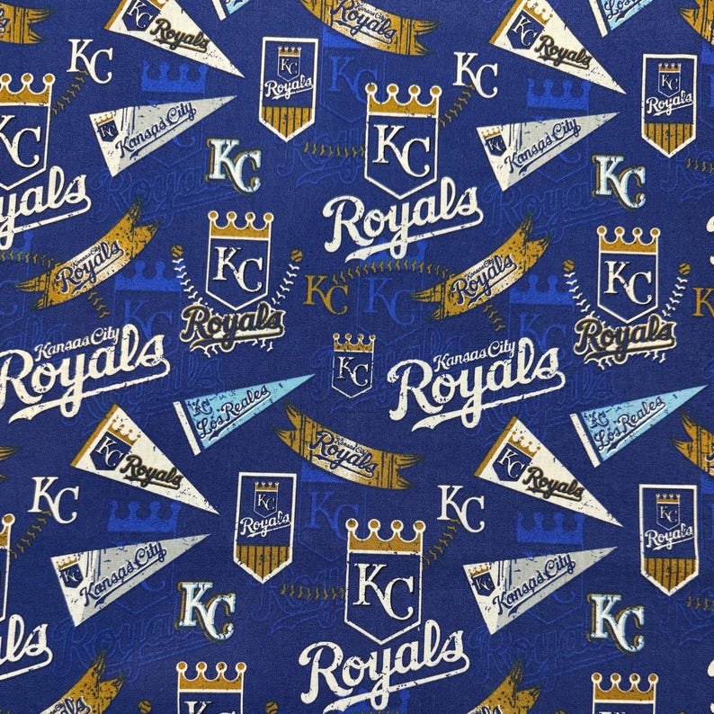 May include: A blue fabric featuring a repeating pattern of Kansas City Royals baseball team logos, pennants, and text. The design includes the team's "KC" logo, crowns, and the word "Royals" in white and gold.
