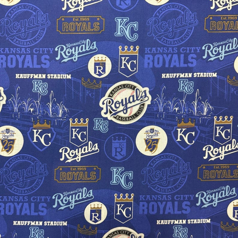 May include: A blue fabric featuring various Kansas City Royals baseball team logos and text. The design includes the team name, "KC" logos, crowns, and the Kauffman Stadium illustration. The fabric has a repeating pattern.