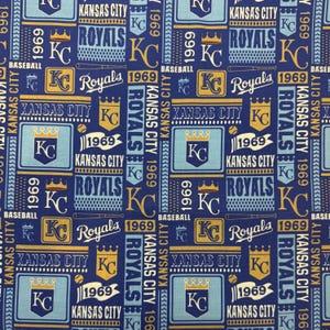 May include: A repeating pattern fabric featuring the Kansas City Royals baseball team. The design includes the team's logo, the text "Royals", "Kansas City", and the year "1969" in blue, gold, and white on a navy blue background.