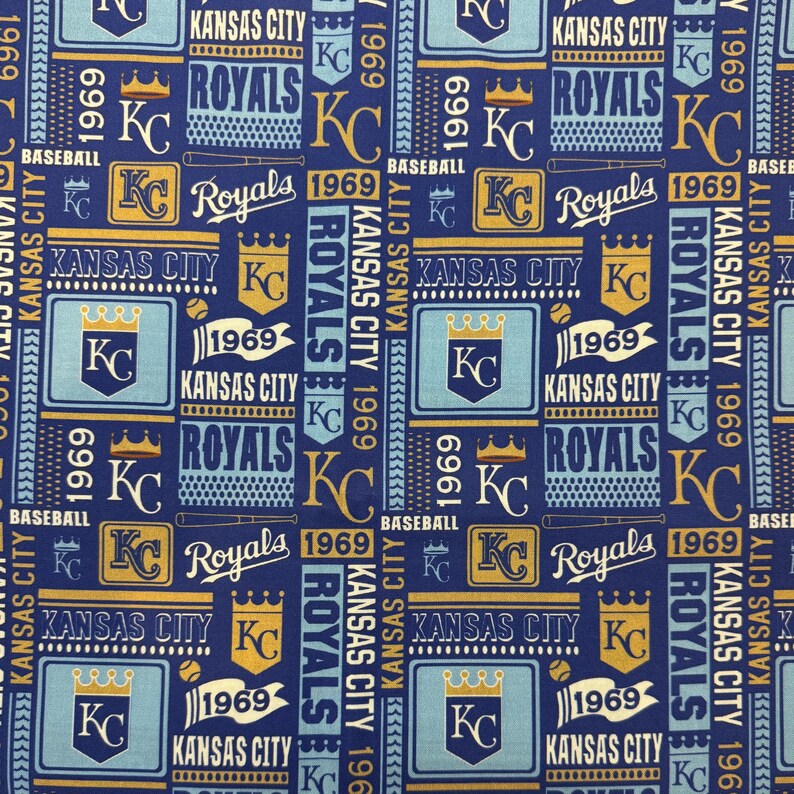 May include: A repeating pattern fabric featuring the Kansas City Royals baseball team. The design includes the team's logo, the text "Royals", "Kansas City", and the year "1969" in blue, gold, and white on a navy blue background.