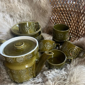 Può includere: Una teiera e tazze in ceramica verde con un motivo geometrico. Il set è su un tappeto bianco soffice.