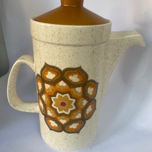 May include: A white ceramic coffee pot with a brown lid and a geometric pattern in shades of brown, orange, and yellow.
