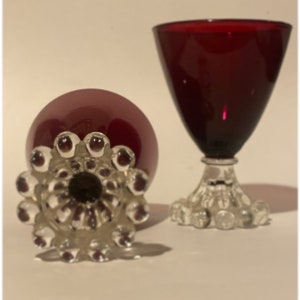May include: Two ruby red stemmed glasses with clear glass bases. The bases have a decorative pattern of small clear glass balls.