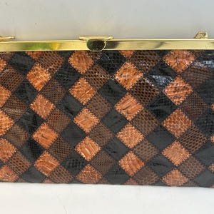 Peut inclure: Une pochette rectangulaire avec un fermoir et un cadre dorés. L'extérieur du sac présente un motif patchwork de pièces en forme de losanges marron, noires et beiges, créant un motif texturé. Le sac semble être en cuir.