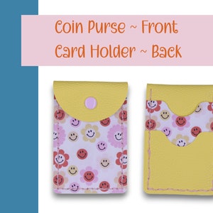May include: A yellow coin purse with a pink button and a white background with a pattern of pink and red smiley faces and flowers. The back of the purse is yellow with a pocket for cards.