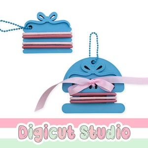 Peut inclure: Deux supports en plastique bleu en forme de boîtes cadeaux avec des nœuds, chacun doté d'une chaînette à billes bleue. Les supports sont entourés d'élastiques à cheveux dans des tons rose et mauve. Un support inclut un ruban rose clair noué.