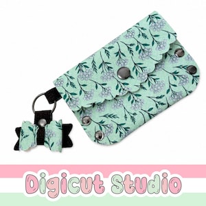 May include: A mint green rectangular pouch with a scalloped flap and a floral pattern of white flowers and dark green leaves. The pouch features silver metal snaps and is attached to a black metal keyring with a small matching bow charm.