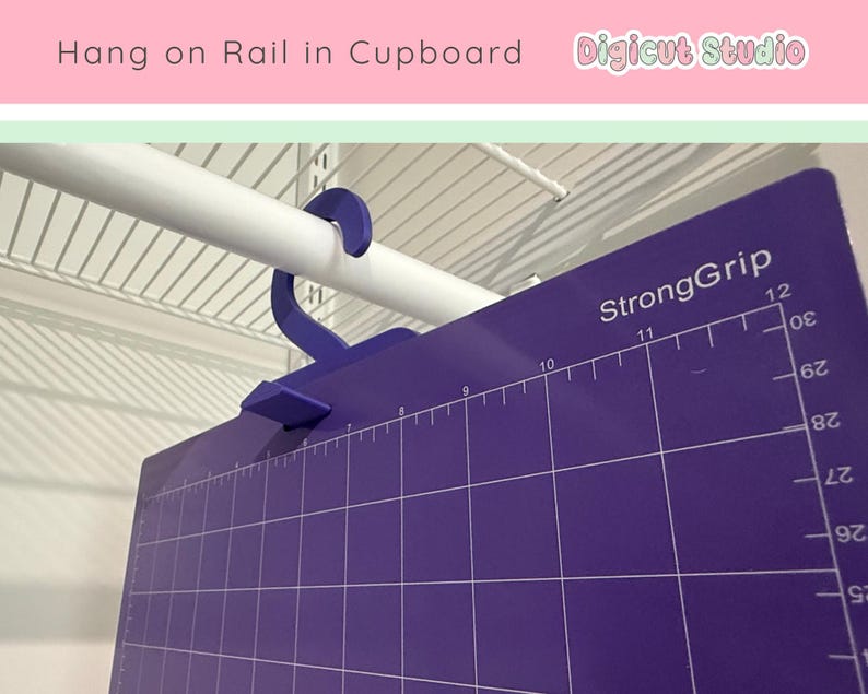 May include: A purple cutting mat with a grid pattern and measurement markings, hanging from a white closet rod. The mat has the text "StrongGrip" and numbers indicating inches. A blue hanger is used to suspend the mat.