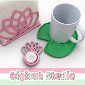 May include: A pink lotus flower-shaped napkin holder, a matching tealight candle holder, and two green lily pad-shaped coasters. A white mug sits on one of the coasters. The text "Digicut Studio" is at the bottom.