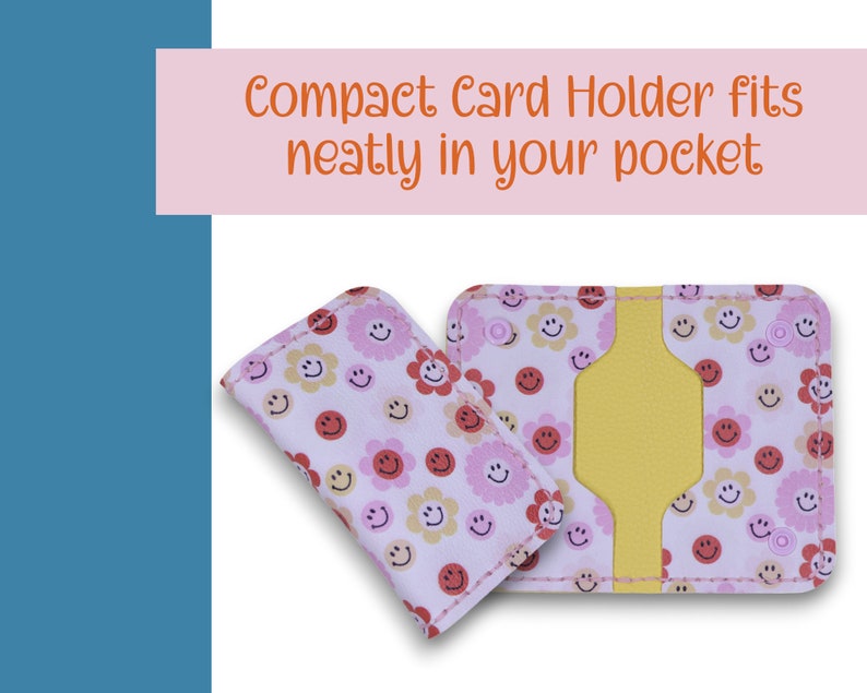 May include: A pink card holder with a yellow interior and a pattern of pink and yellow flowers and smiley faces. The text "Compact Card Holder fits neatly in your pocket" is printed above the card holder.