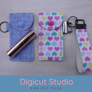 May include: Three keychains with different fabric patterns. The first keychain is blue with a pink lipstick inside. The second keychain is white with pink, blue, and green hearts. The third keychain is white with pink, blue, and green hearts and a black strap. The keychains are labeled "Digicut Studio SVG Cut Files".