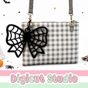 May include: A rectangular crossbody bag featuring a grey and white gingham pattern with a detachable black acrylic bow charm shaped like a spider web. The bag includes a grey adjustable strap attached with silver-toned metal hardware clips.