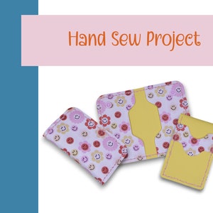 May include: Three hand-sewn wallets with a yellow fabric exterior and a pink and white fabric interior with a smiley face and flower pattern. The wallets are for holding cards and cash.