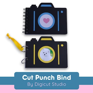 Può includere: Due album fotografici a forma di macchina fotografica nera con accenti gialli e blu. L'album superiore ha un cuore rosa nel mirino. L'album inferiore ha una foto di un cane bianco nel mirino. Gli album sono etichettati "Cut Punch Bind" e "By Digicut Studio".