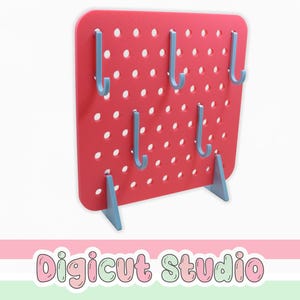 Puede incluir: Un tablero perforado rojo con agujeros espaciados uniformemente y seis ganchos azules. El tablero está soportado por dos soportes triangulares azules. El texto "Digicut Studio" está en la parte inferior de la imagen.