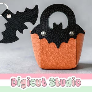 May include: A Halloween-themed set featuring a small orange and black purse with a bat design and a black bat keychain. The purse has a handle and is decorated with silver rivets. The text "Digicut Studio" is at the bottom.