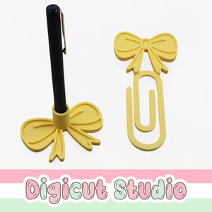 May include: A yellow bow-shaped pen holder with a black pen and a yellow bow-shaped paperclip. The pen holder has a circular base to hold the pen. The paperclip is a large, decorative version of a standard paperclip.