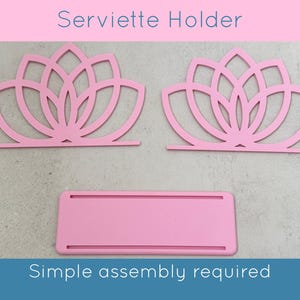 May include: Pink Serviette Holder with a lotus flower design. The holder is made of cut-out shapes and includes the text "Serviette Holder" and "Simple assembly required". The holder is designed to hold napkins.