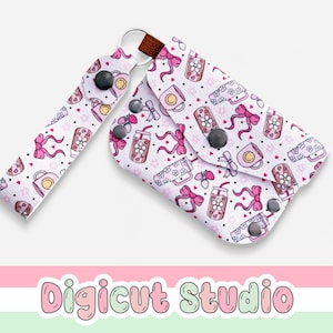 Puede incluir: Un llavero blanco y un juego de pulsera con un patrón repetido de lazos rosas, tazas de café y bebidas. El llavero tiene un cierre de botón a presión y un lazo de cuero marrón. La pulsera tiene un botón a presión negro.