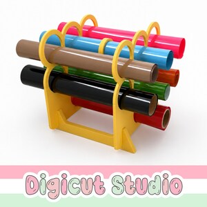 May include: A yellow plastic storage rack holding multiple rolls of vinyl in various colors including pink, blue, brown, green, black, and red. The text Digicut Studio is displayed in a bubble font at the bottom of the image.