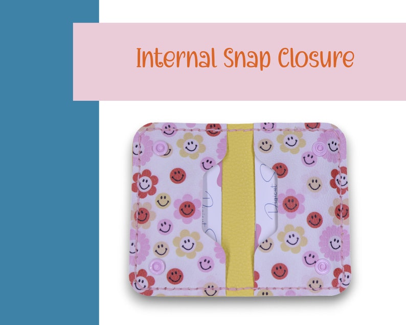 May include: A white leather card holder with a pink and yellow smiley face pattern. The card holder has a yellow elastic band and a snap closure.