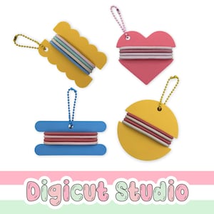 May include: Four colorful plastic organizers with ball chains, each wrapped with elastic hair ties. The shapes include a yellow scalloped spool, a pink heart, a blue rectangular spool, and a yellow circle. The text Digicut Studio is at the bottom.