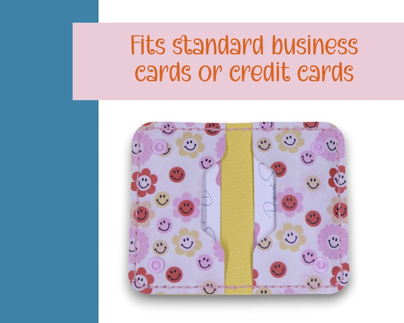 May include: A pink and white card holder with a smiley face and flower pattern. It has a yellow divider and fits standard business cards or credit cards.