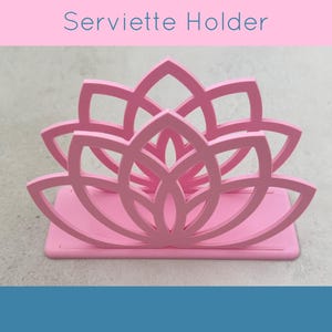 May include: A pink serviette holder with a lotus flower design. The holder is made of a solid material and has a rectangular base. The text "Serviette Holder" is displayed above the holder.