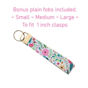 May include: A white key chain with a floral pattern and gold hardware. The key chain is 1 inch wide and comes with three plain fobs in small, medium, and large sizes.