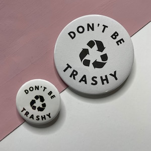 May include: Two white round buttons with black text and a recycling symbol. The larger button says "Don't Be Trashy" and the smaller button says "Don't Be Trashy".