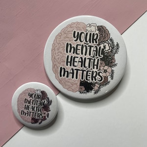 May include: Two round buttons with a white background and a pink and black brain illustration. The text "Your Mental Health Matters" is printed in black on the buttons.