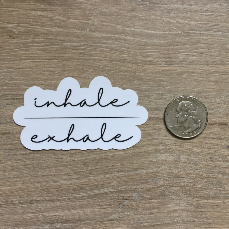 May include: A white sticker with the words "inhale exhale" in black cursive script. The sticker is cloud-shaped and is next to a U.S. quarter coin for size comparison.
