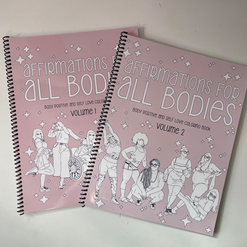 Op de afbeelding: Twee roze spiraalgebonden kleurboeken met de titel "Affirmations for All Bodies" en de woorden "Body Positive and Self Love Coloring Book". Het eerste boek is Volume 1 en het tweede boek is Volume 2.