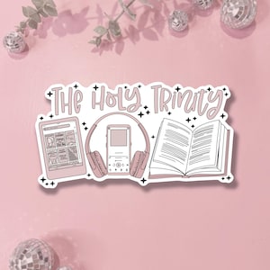 May include: A die-cut sticker featuring the text "The Holy Trinity" in a light pink script font. The design includes a digital e-reader, a music player with headphones, and an open book, all accented with small black star icons on a white background.
