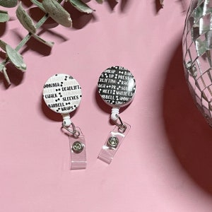 May include: Two white retractable badge holders with black text. The left badge holder has the text "LIGHTS ML AMMONIA DUMBB NGLET DEADLIFT CHALK CONJUGAT NOW SLEEVES BARBELL AMR WRAPS". The right badge holder has the text "BER AMRAP BARD SUPPRESS ERLIFTING RAC ACH PR SOUNT MEET WHITE LIO MBBELL AMMO ETSING".