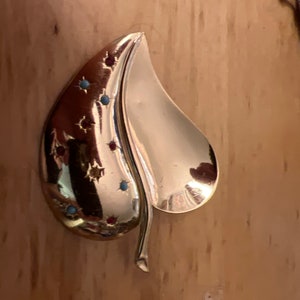 May include: A gold-toned leaf-shaped brooch with red, blue, and turquoise gemstones set in a starburst pattern.