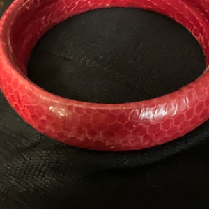 Puede incluir: Un brazalete de cuero rojo con un patrón texturizado.