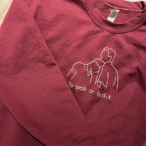 Puede incluir: Sudadera color burdeos con un dise&ntilde;o bordado en blanco de tres figuras y el texto "to speak or to die".