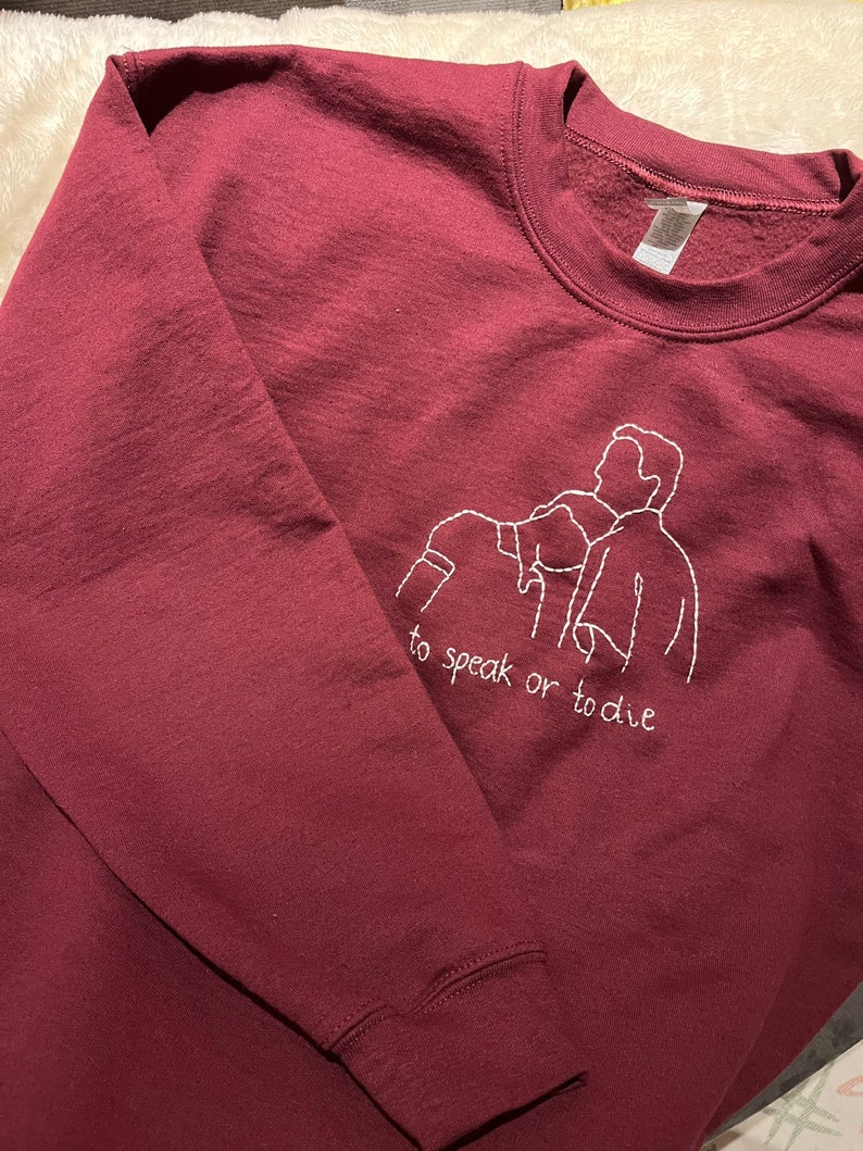 Puede incluir: Sudadera color burdeos con un dise&ntilde;o bordado en blanco de tres figuras y el texto "to speak or to die".